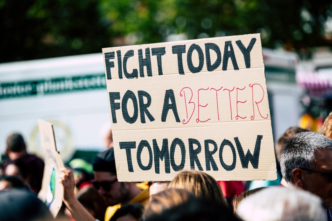 heros-img Crowd holding a protest sign with 'Fight Today for a Better Tomorrow', outdoors and during the day.