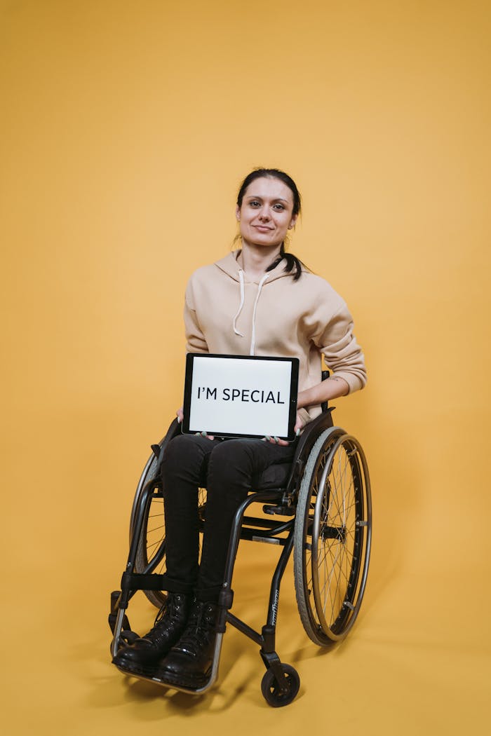 our-story Woman in wheelchair holding a digital tablet with a motivational message on a yellow background.