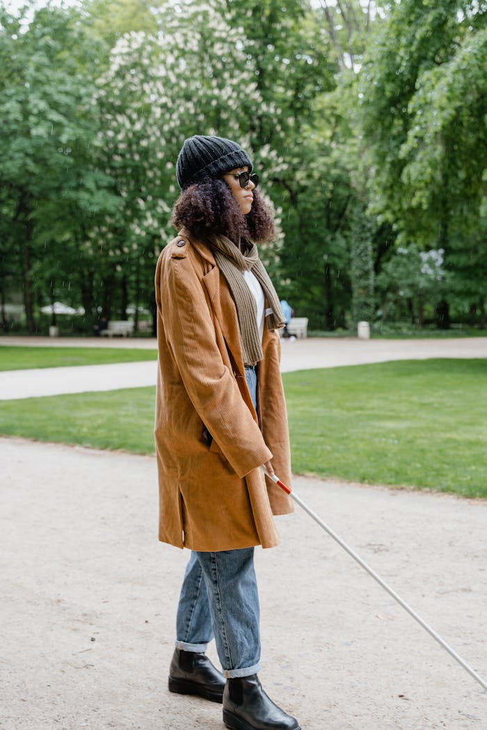 who-we-are A blind woman using a white cane walks confidently in a park, showcasing independence.